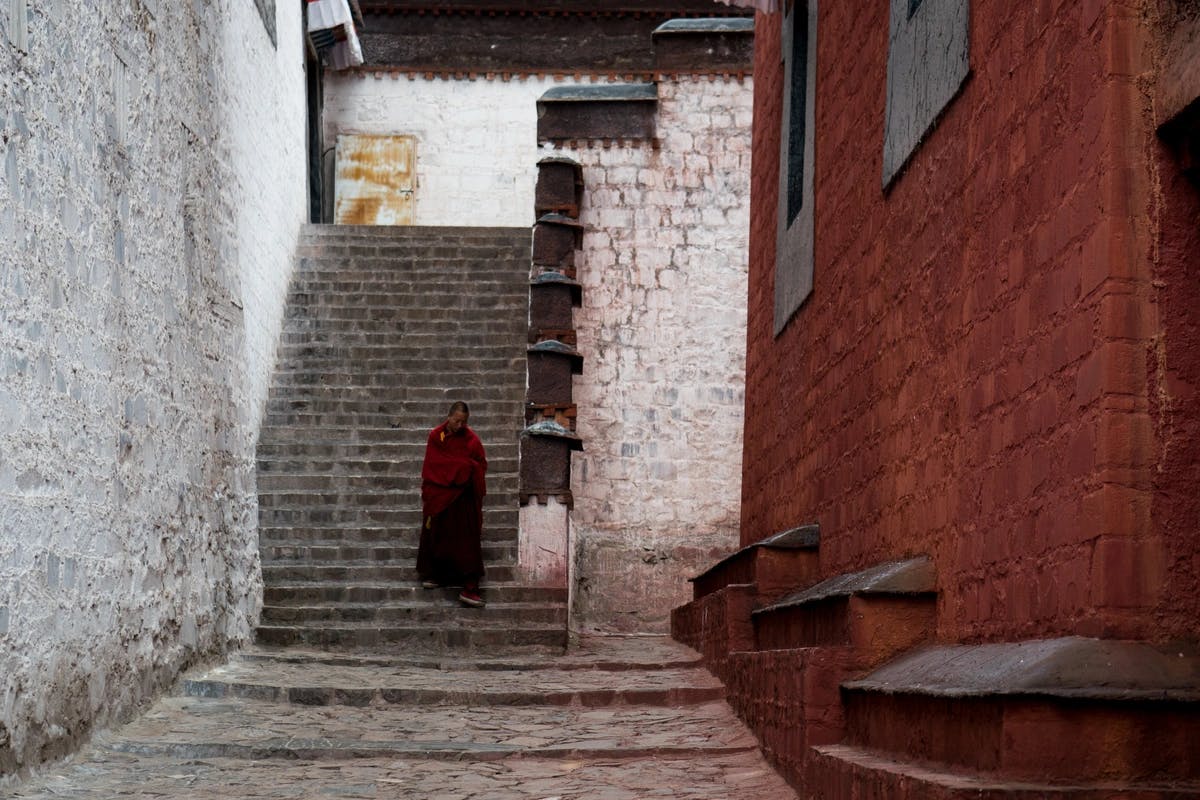 person in long red garment walks down stairs in a brick alleyway